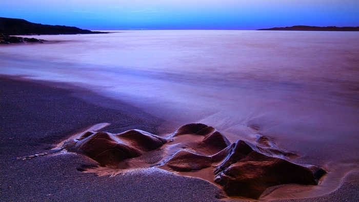 Beach with rocks and calm ocean at twilight