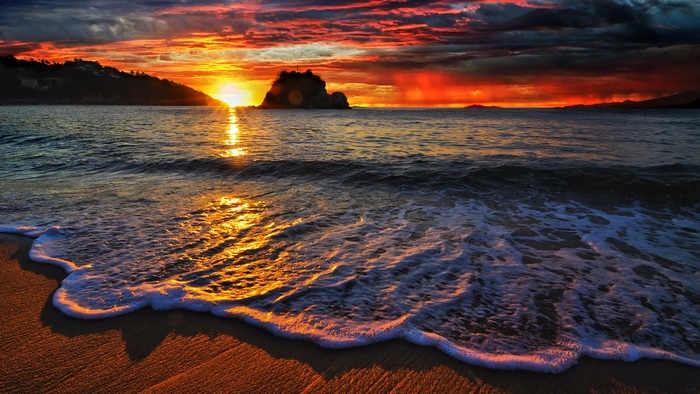 Sunset over the ocean with waves crashing on the beach