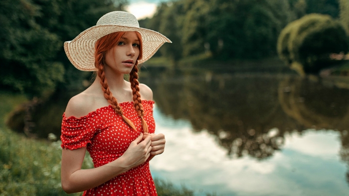 Redhead woman in a red polka dot dress and hat by the water