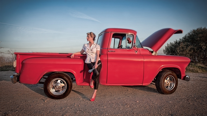 Woman with wrench leaning on red classic truck