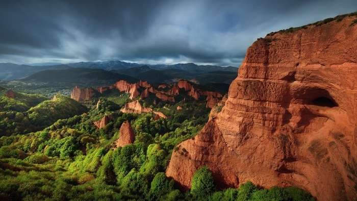 Red rock formations and green hills under cloudy sky