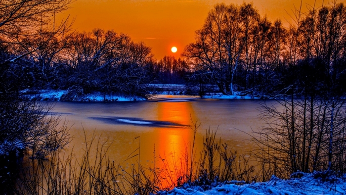Winter sunset over a frozen lake with trees