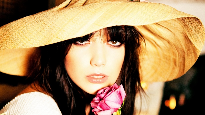Woman in a wide-brimmed hat holding a pink rose