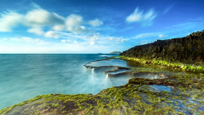 Rocky coastline with moss and ocean under blue sky
