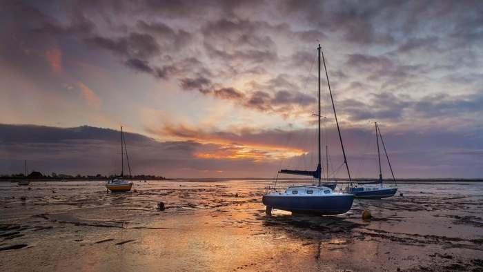 Sailboats on a muddy shore at sunset