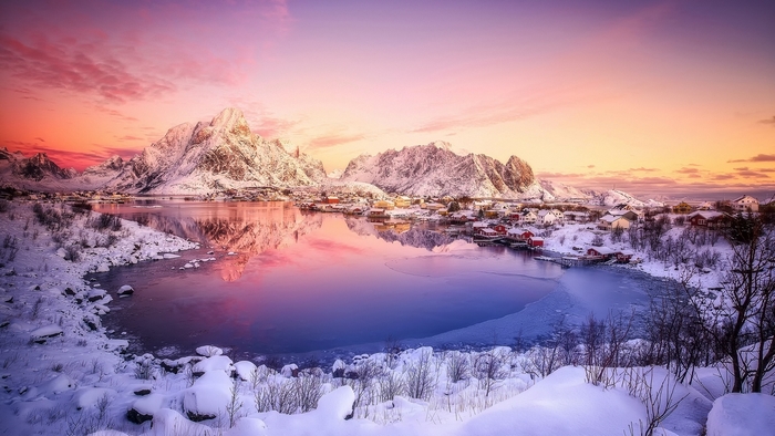 Snowy village by mountains and lake at sunset