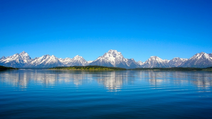 Snow-capped mountains reflected in a calm lake under a clear blue sky