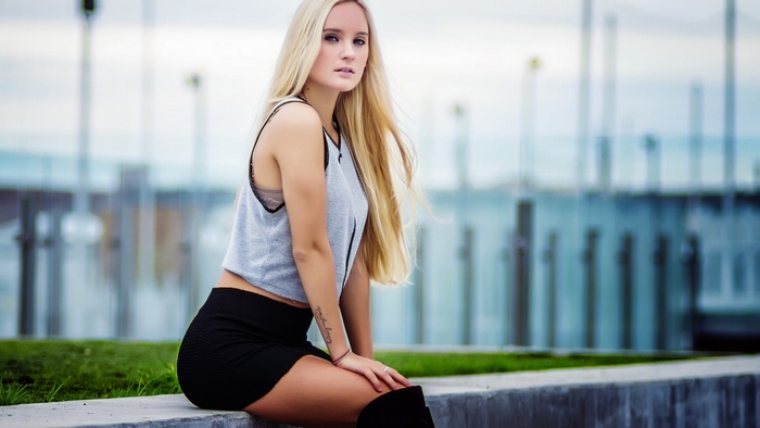 Woman with blonde hair wearing a grey tank top and black skirt