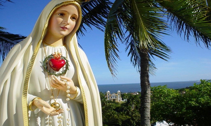 Statue of the Immaculate Heart of Mary with a church and ocean in the background
