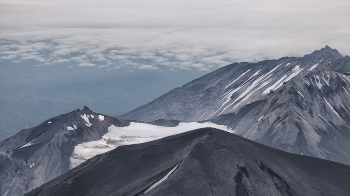 Volcanic mountain range with snow patches under cloudy sky