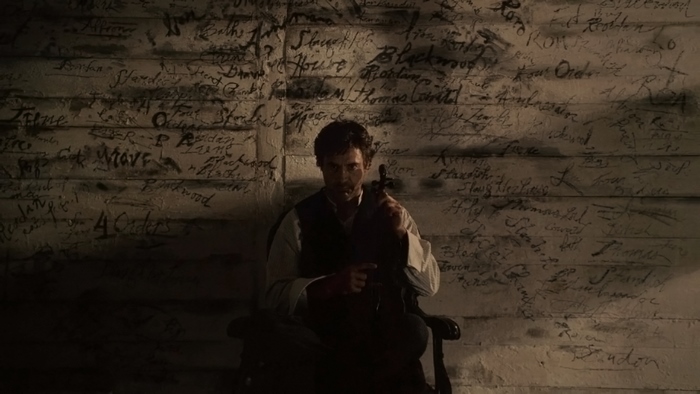 Man playing violin in front of a wall with writing