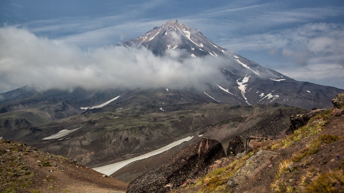 Volcano shrouded in clouds with rocky foreground