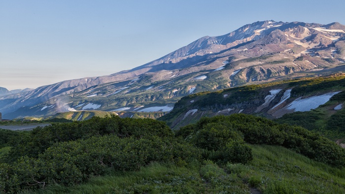Volcanic mountain landscape with snow patches and green bushes