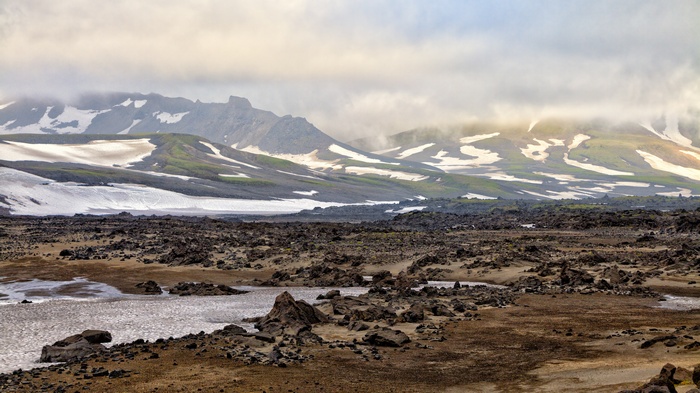 Volcanic landscape with snow-capped mountains under cloudy sky