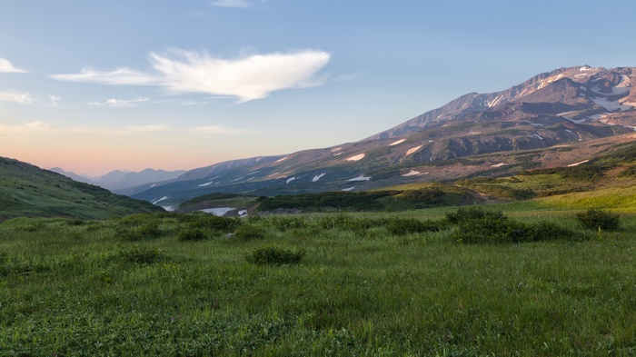 Mountain landscape with green fields and snow patches