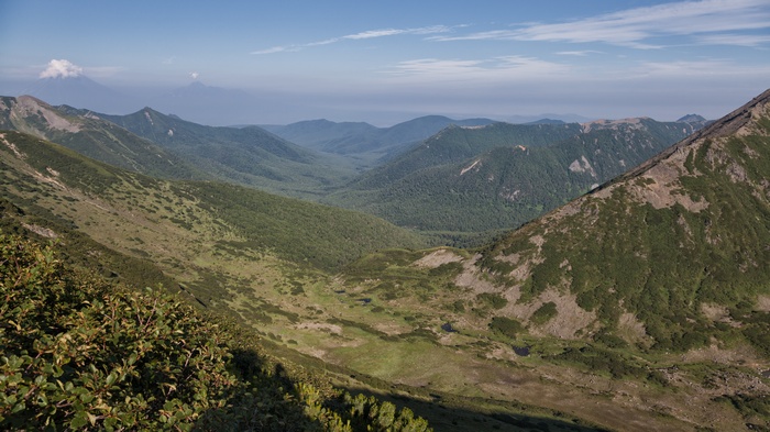 Mountain valley with distant volcanoes under a blue sky