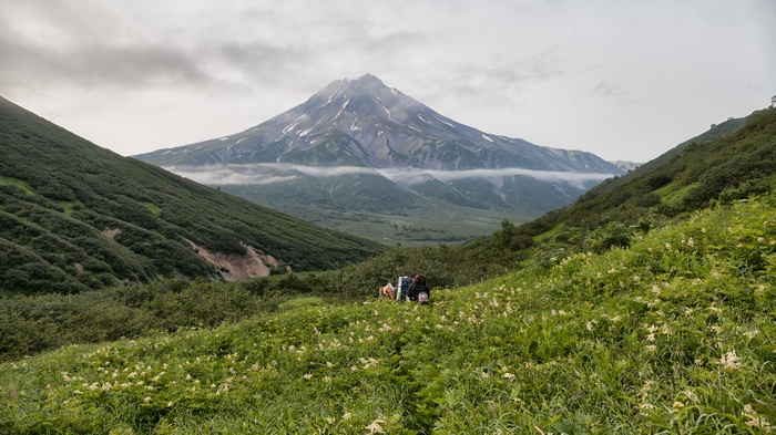 Hikers resting in a mountain valley with a volcano in the background