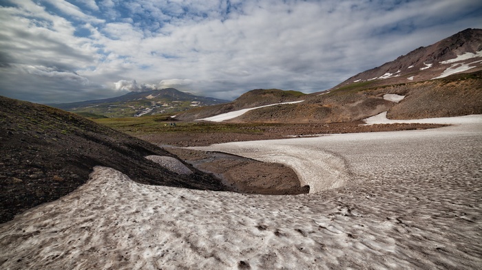 Volcanic landscape with snow patches and distant mountains