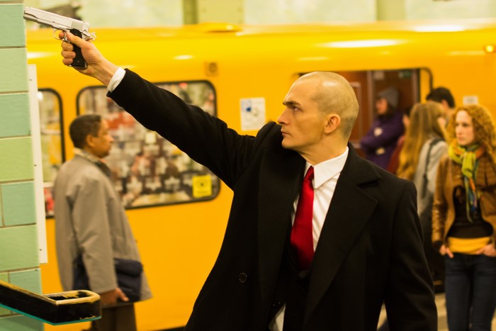 Agent 47 with a gun in a subway station