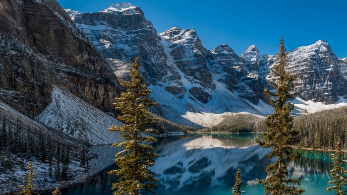 Snow-capped mountains reflected in a turquoise lake with pine trees