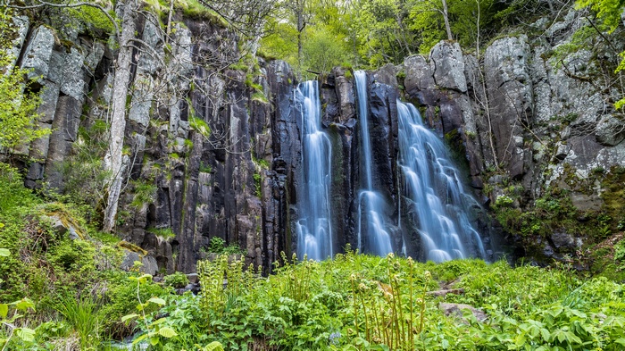 Waterfall cascading over dark rocks surrounded by greenery