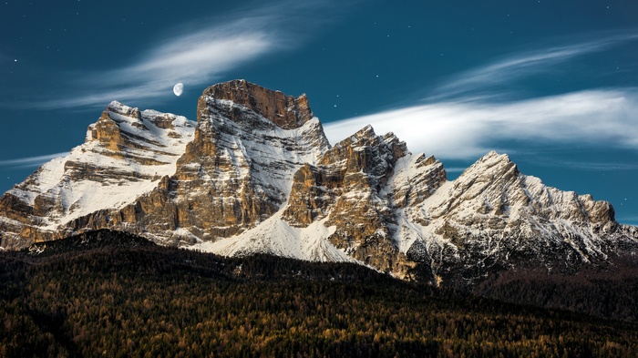 Snow-capped mountains under a starry night sky with moon