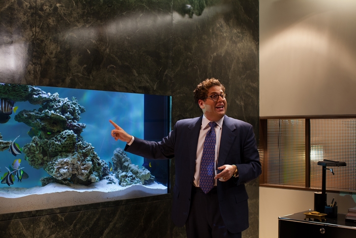 Jonah Hill in a suit pointing at a fish tank