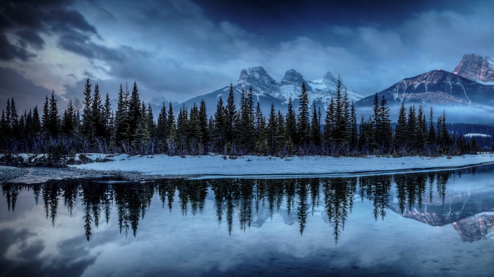 Three Sisters mountains reflected in a calm lake with pine trees