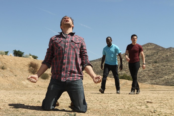 Man kneeling in desert with two men behind him