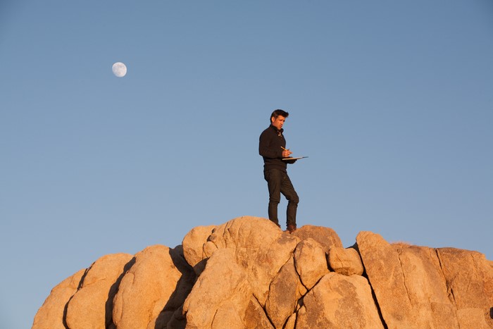 Man on rocks with moon in sky