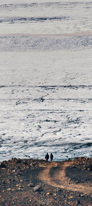 Two people on a rocky shore overlooking a glacier