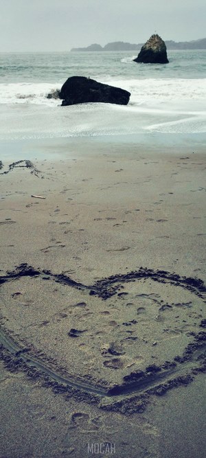 Heart drawn in sand on a beach with rocks in the ocean