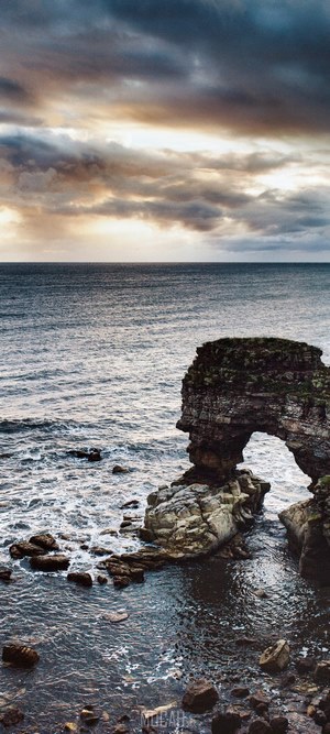 Rocky Archway in the Ocean Under Cloudy Sky