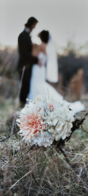 Wedding couple embracing with bouquet in grass