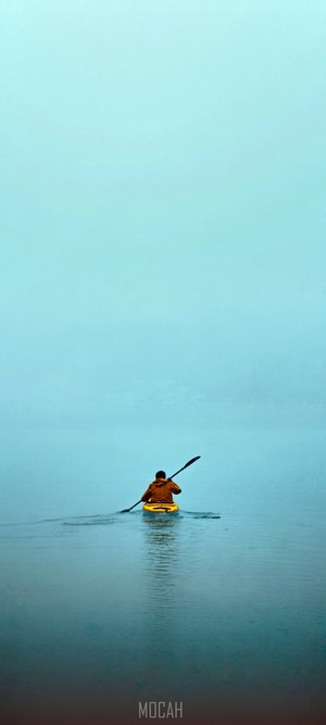 Person kayaking on a foggy blue lake
