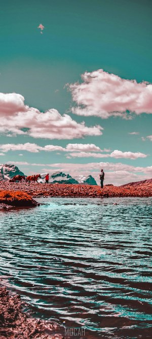 People and horses by a lake with mountains