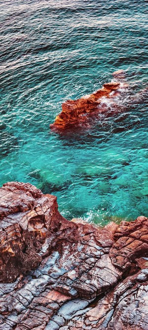 Turquoise sea water crashing on rocky shore