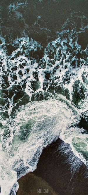 Aerial view of ocean waves crashing on a dark shore
