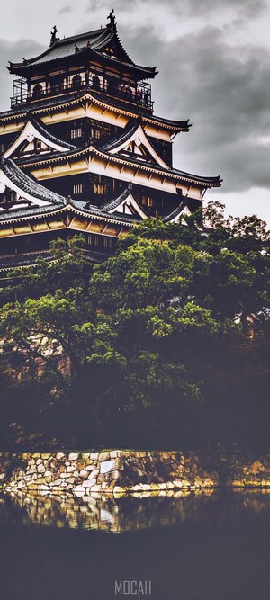 Japanese castle on a hill with trees and water
