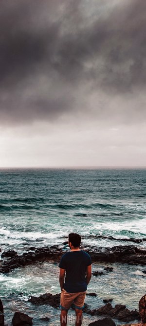 Man looking at the ocean under stormy clouds