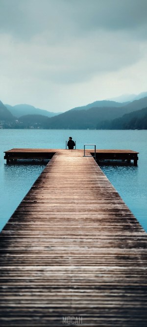 Person sitting on a wooden pier overlooking a lake and mountains
