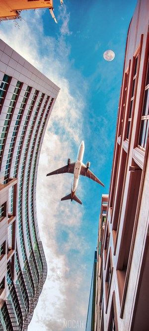 Airplane flying between modern buildings with moon in sky