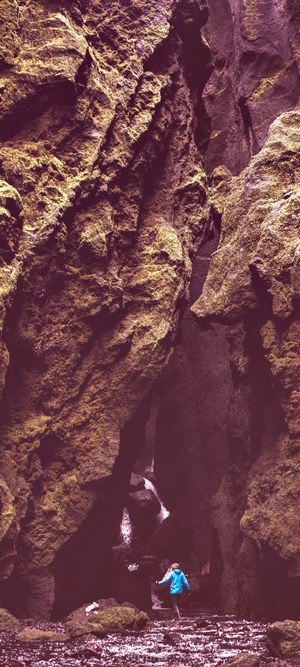 Person walking through a mossy canyon with a waterfall