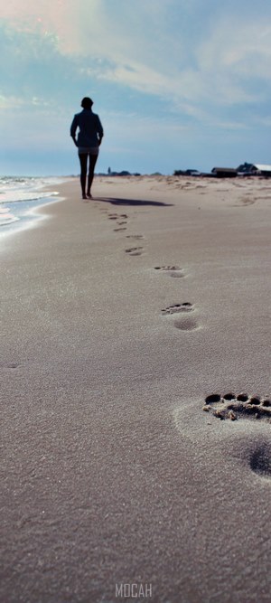 Woman walking on a sandy beach leaving footprints