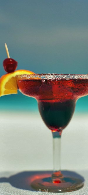Red cocktail with orange slice and cherry on beach
