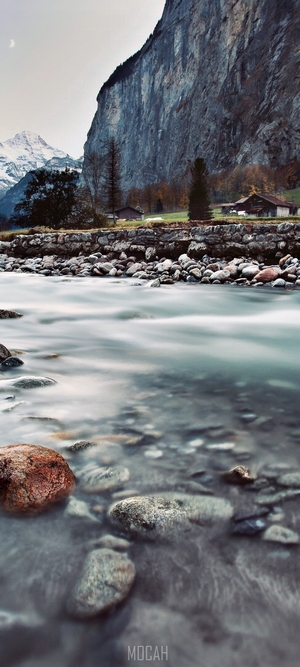 River flowing past rocks with a mountain cliff and village