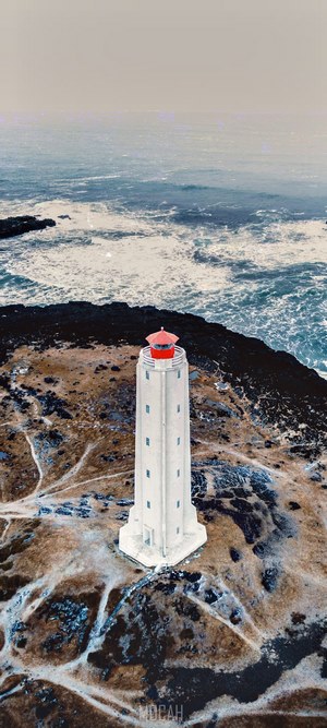 White lighthouse on a rocky coast with rough seas