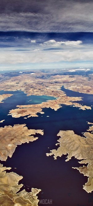 Aerial view of a vast lake with dry, rugged coastlines under a cloudy sky
