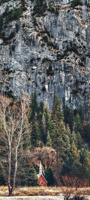Red chapel in front of a rocky mountain and forest