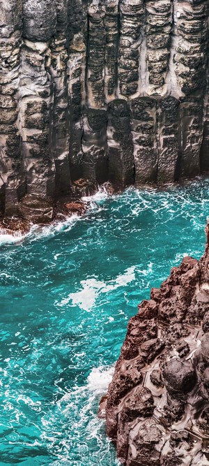 Turquoise water flows between basalt columns on a rocky coast